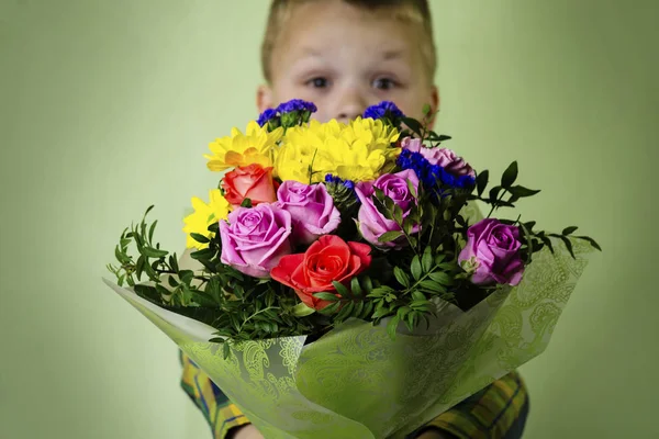 緑の背景に花の美しい花束を持つ面白い少年 — ストック写真