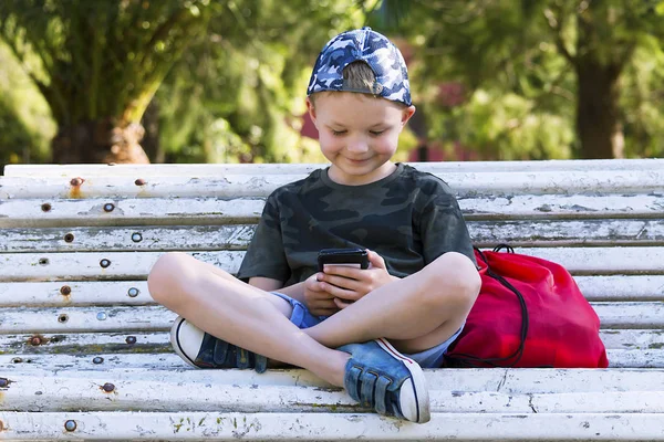 Симпатичный Мальчик Ищет Мобильный Телефон Скамейке Летом — стоковое фото