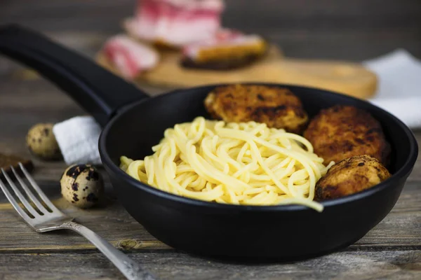 Spaghetti with meat cutlets in a frying pan on a wooden board