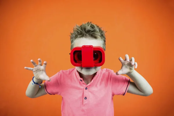 面白い少年は明るいオレンジ色の背景に電話のための仮想現実のメガネで再生します — ストック写真