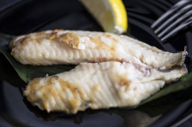 koyu bir arka plan üzerinde bir tabak üzerinde limon ile kızarmış deniz balığı levrek fileto