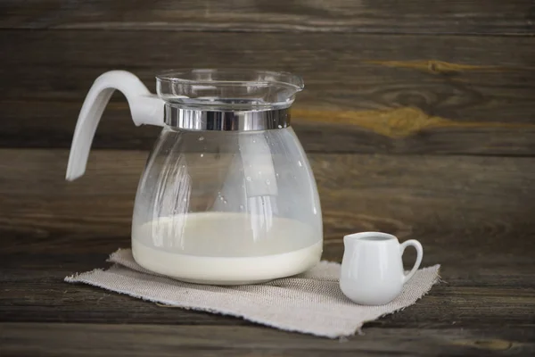 large glass jug with milk and a small ceramic jug on an old wooden background