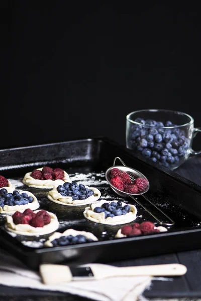cookies from puff pastry with raspberries and blueberries on a baking sheet on a dark background
