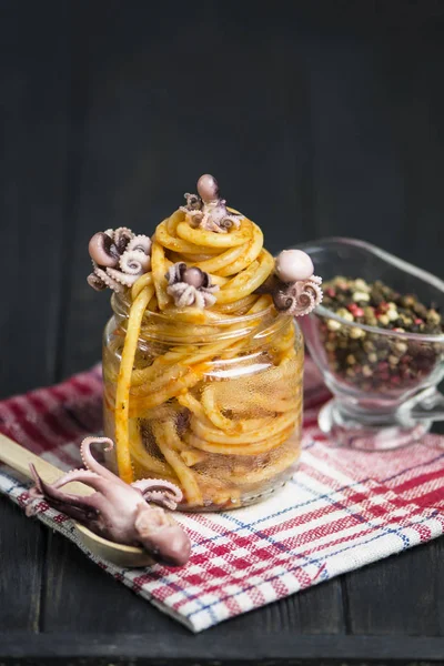 pasta with tomato sauce and octopus in a glass jar on a dark background