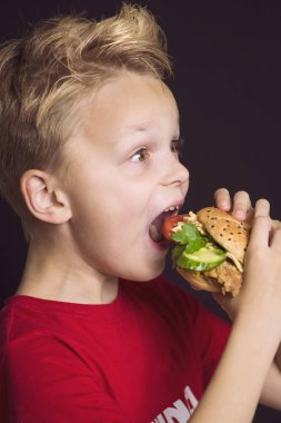 Kapalı ağızlı komik çocuk tavuk, sebze ve peynirli lezzetli bir burger yiyor.
