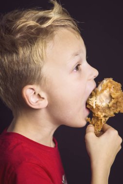 Komik çocuk, ağzı açık, iştah açıcı tavuk budu yiyor.