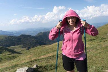 Giovane ragazza con una vistosa felpa rosa sorride durante una escursione sulle montagne in una soleggiata giornata primaverile
