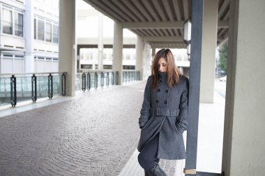 Giovane ragazza dai lunghi capelli castani si mette in posa sotto al portico di una costruzione cittadina
