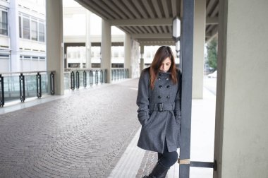 Giovane ragazza dai lunghi capelli castani si mette in posa sotto al portico di una costruzione cittadina