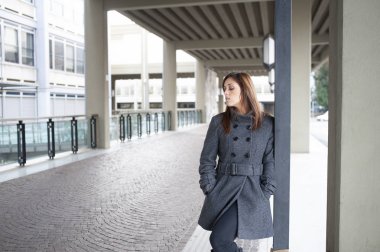 Giovane ragazza dai lunghi capelli castani si mette in posa sotto al portico di una costruzione cittadina