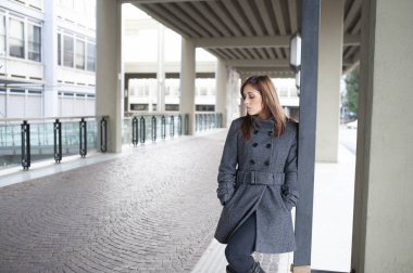Giovane ragazza dai lunghi capelli castani si mette in posa sotto al portico di una costruzione cittadina