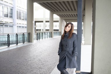 Giovane ragazza dai lunghi capelli castani si mette in posa sotto al portico di una costruzione cittadina
