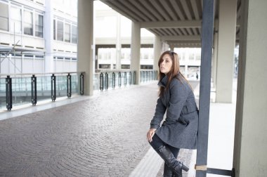 Giovane ragazza dai lunghi capelli castani si mette in posa sotto al portico di una costruzione cittadina