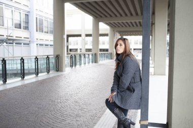 Giovane ragazza dai lunghi capelli castani si mette in posa sotto al portico di una costruzione cittadina