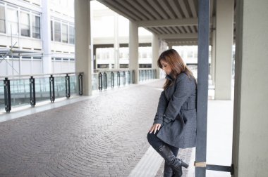 Giovane ragazza dai lunghi capelli castani si mette in posa sotto al portico di una costruzione cittadina