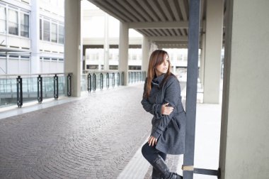 Giovane ragazza dai lunghi capelli castani si mette in posa sotto al portico di una costruzione cittadina