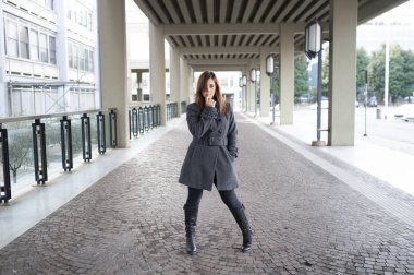 Giovane ragazza dai lunghi capelli castani si mette in posa sotto al portico di una costruzione cittadina