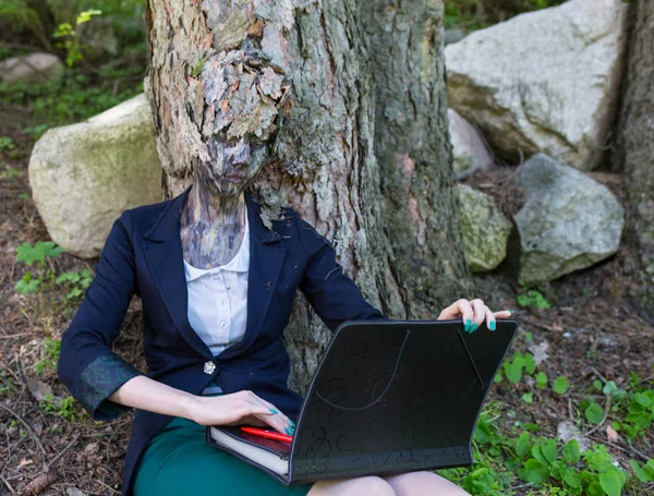 Travailleuse de bureau en costume d'entreprise, à l'extérieur avec un maquillage sur le visage imitant l'écorce d'un arbre. La fille fusionne avec le tronc de l'arbre, s'assied et se repose sur lui . — Photo