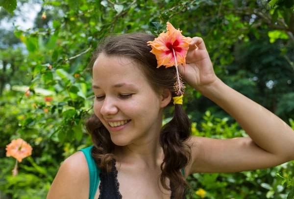 Dziewczyna w parku, uśmiechając się i zasłania twarzy z kwiatem — Zdjęcie stockowe