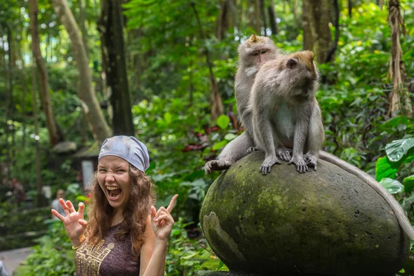 Joven mujer caucásica posando para una foto con mono lindo en el hombro. El curioso macaco se acerca a la chica viajera saltando sobre su hombro. Mujer feliz tomando una foto divertida con un mono pequeño . — Foto de Stock