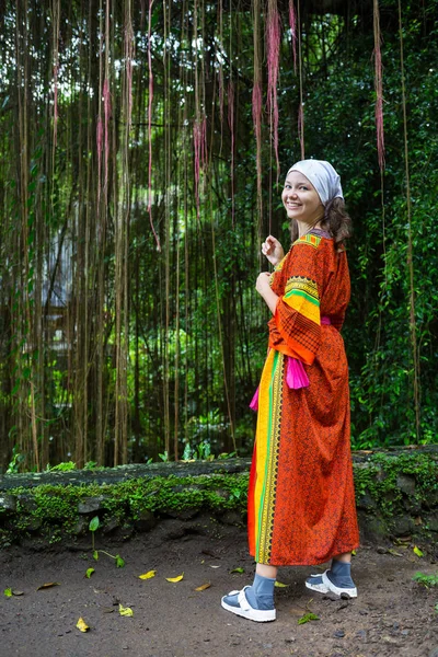 Belle fille sauvage en robe rose pâle, avec des boucles noires assises dans l'herbe au milieu de la jungle. Hamac fait d'herbe et de fleurs. Femme tropicale avec fleur. Hanche tonifiante, couleur créative — Photo