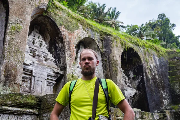 古代の神聖な王墓グヌン ・ カウィの前に一人で立っている男の背面します。男は服を着ての伝統的なサロンと白のトップです。周り誰も。男に選択と集中。バリを探索します。 — ストック写真