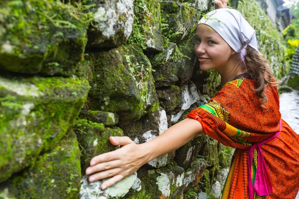 Een vrouw in een jurk is een bakstenen muur klimmen. Het meisje klimt op een stenen omheining. Klimmer op een stad straat. De muur van de oude verwoeste gebouw. — Stockfoto