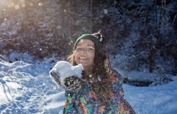 Весёлая зимняя веселая женщина бросает снежное знамя. Девочка, играющая на улице в снегу, смеется в желтом пальто, шляпе, перчатках и шарфе . — стоковое фото