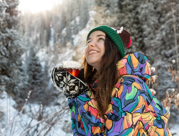 Девушка наслаждается снегопадом. Молодая женщина в трикотажной форме пьет чай в лесу во время снегопада. Тонированное фото — стоковое фото