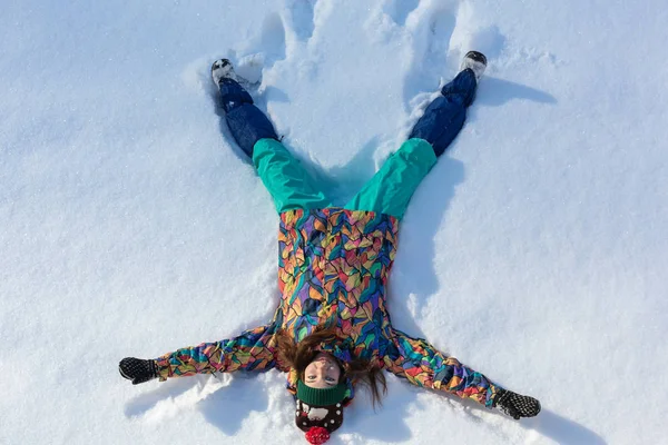Вид под высоким углом счастливой девушки, лежащей на снегу и двигающей руками и ногами вверх и вниз, создавая фигуру снежного ангела. Улыбающаяся женщина лежит на снегу в зимний отпуск с копировальным пространством — стоковое фото