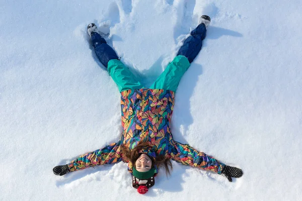 Вид под высоким углом счастливой девушки, лежащей на снегу и двигающей руками и ногами вверх и вниз, создавая фигуру снежного ангела. Улыбающаяся женщина лежит на снегу в зимний отпуск с копировальным пространством — стоковое фото
