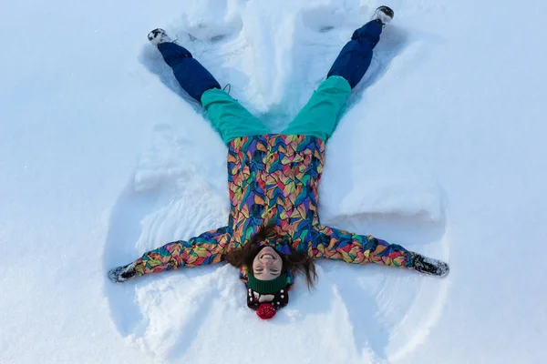 Visão de alto ângulo da menina feliz deitada na neve e movendo seus braços e pernas para cima e para baixo, criando uma figura de anjo da neve. Mulher sorridente deitada na neve nas férias de inverno com espaço de cópia — Fotografia de Stock