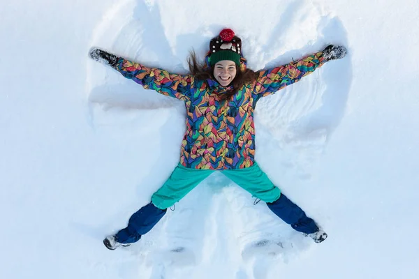 Kar üzerinde uzanan mutlu kızın yüksek açılı görüntüsü ve kollarını ve bacaklarını aşağı yukarı hareket ettirerek bir kar meleği figürü yaratıyor. Kış tatilinde karların üzerinde uzanan gülümseyen kadın fotokopi aletiyle — Stok fotoğraf