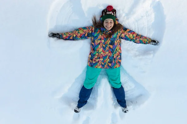 Kar üzerinde uzanan mutlu kızın yüksek açılı görüntüsü ve kollarını ve bacaklarını aşağı yukarı hareket ettirerek bir kar meleği figürü yaratıyor. Kış tatilinde karların üzerinde uzanan gülümseyen kadın fotokopi aletiyle — Stok fotoğraf