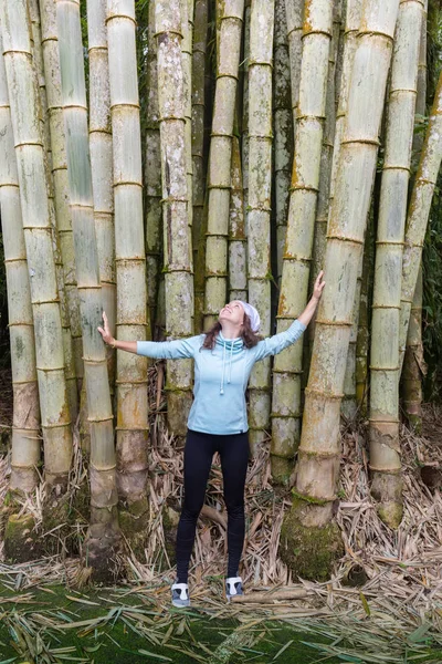 Chica joven con estilo posando contra un árbol de bambú en el parque, descansando —  Fotos de Stock