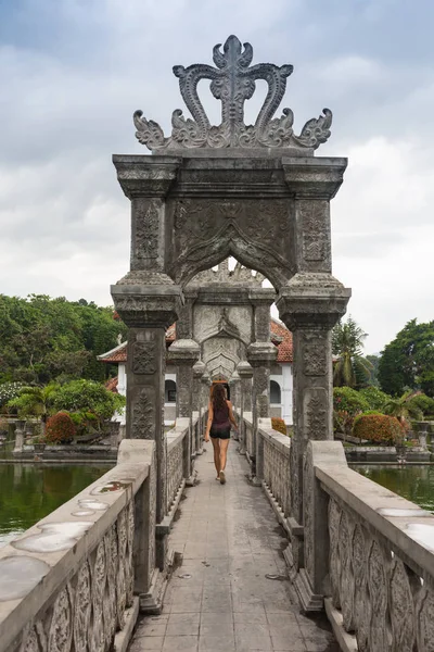 Blond girl walking away on a stone bridge in historical Bali hindu temple, surrounded by water — Stock Photo, Image