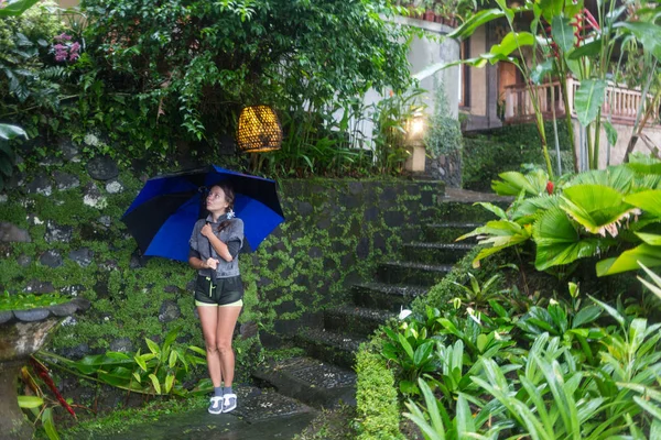 Uma menina está sob guarda-chuvas azuis em uma noite chuvosa, em uma praia tropical em Bali durante a estação chuvosa . — Fotografia de Stock