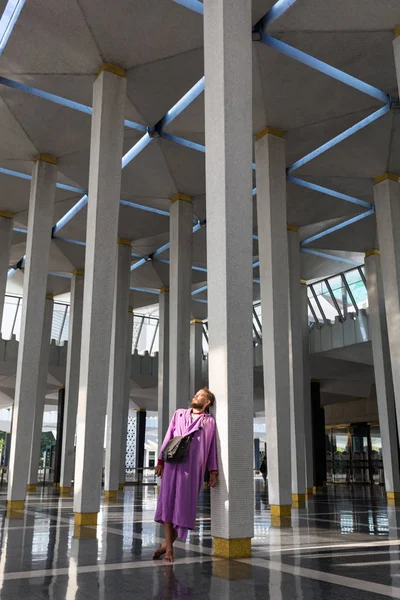 Um turista masculino na mesquita nacional da cidade de Kuala Lumpur fica perto da coluna e goza da beleza do interior . — Fotografia de Stock