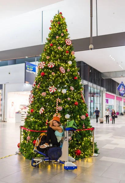 Girl in winter clothes and a backpack cute smiles on the background of a cafe with glass doors and Christmas decorations — Stock Photo, Image