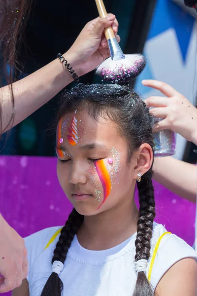 Ałma Ata, Kazachstan - 10 czerwca 2018 r.: Wizażystka niezidentyfikowane dziewczyna sprawia, że twarz jasny karnawał malarstwo do uczestników festiwalu na imprezie Yarkokros, w pobliżu stadionu Almaty Arena 10 czerwca — Zdjęcie stockowe