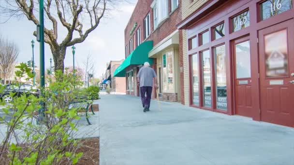 引退した高齢者は 春の日曜日の朝にノースカロライナ州ヘンダーソンビルのダウンタウンのメインストリートを歩いて運動をする — ストック動画