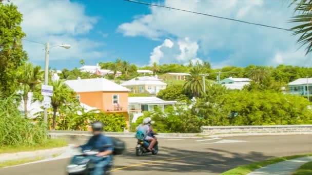 バミューダのサンディス教区の村の通りを走る車とスクーターは 背景に丘の上に鮮やかな色とバミューディアンハウスの建築と晴れた日に — ストック動画