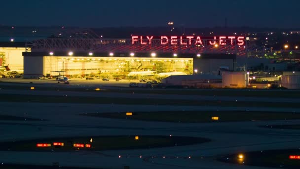 デルタ航空格納庫での夜間 フライデルタジェットサインとハーツフィールド ジャクソン アトランタ国際空港から離陸する民間旅客機 — ストック動画