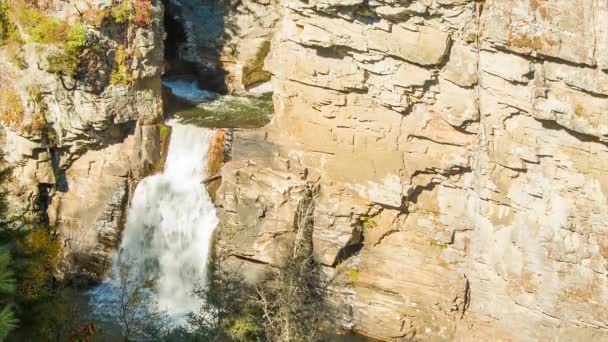 ノースカロライナ州のリンビルの滝を傾け 晴れた日に秋の色の木で頂上から見て滝を見る訪問者に向かって岩壁を渡す — ストック動画