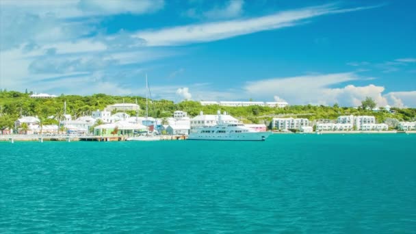 ホテルの建物を備えた豪華なヨットをフィーチャーした晴れた日に熱帯ターコイズブルーの海のフェリーでバミューダのセントジョージ港を出発 — ストック動画