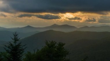 Batı Kuzey Carolina'da Asheville yakınlarındaki Appalachian Dağları'nın Karanlık Katmanları Üzerinde Alacakaranlıkta Moody Sahnesi Orman Üzerinde Bulutlar Aydınlatan Altın Güneş ışınları featuring