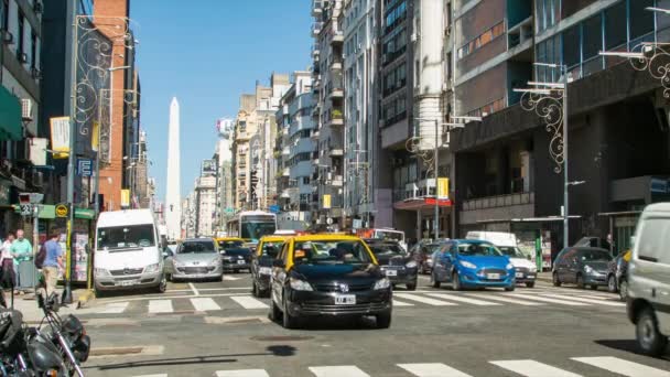 ブエノスアイレスアルゼンチンのブエノスアイレス市内のコリエンテス通りを走行する車両は オベリスコのランドマークを背景に晴れた日に — ストック動画