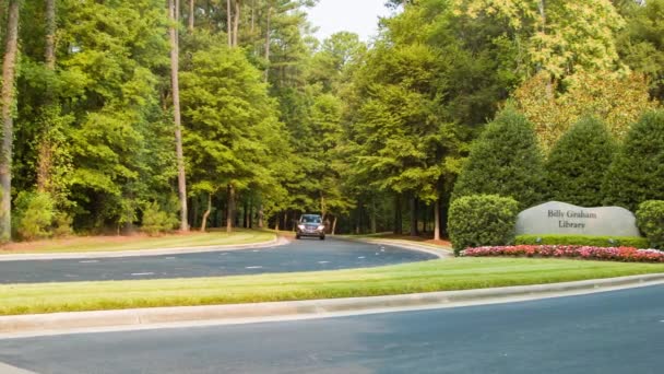 ノースカロライナ州のアトラクションへの訪問者を歓迎する庭の看板を過ぎて運転する車両とシャーロットNcのビリーグラハム図書館の外側の入り口 — ストック動画