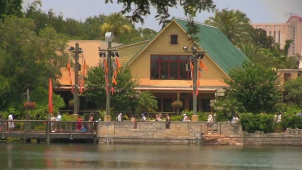 オーランドのシーワールドアドベンチャーパークを訪れる人々は 公園のレストランや建物の前のウォーターフロントに沿って歩いています カメラズームアウト湖と葉を明らかにし ズームイン — ストック動画