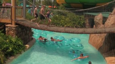 Orlando's Aquatica Su Parkı'nda Tropikal Temalı Tembel Nehir, Orta Florida'da Sıcak Yazlar Günü bir Hang Köprüsü altında akan.